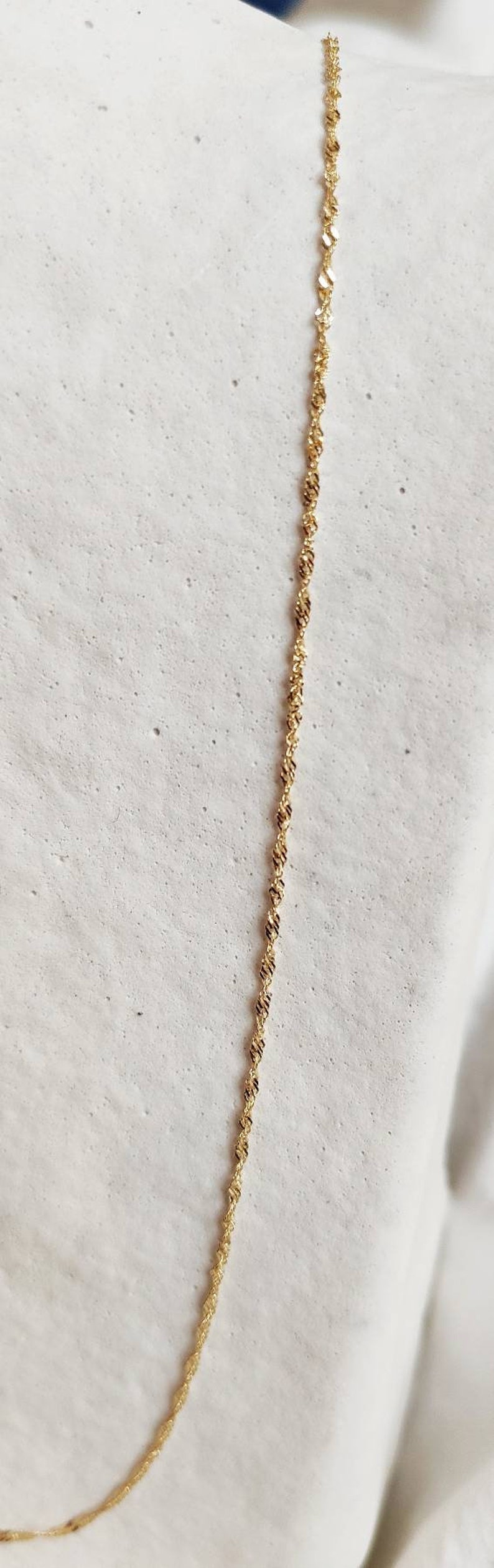 May include: A gold chain necklace with a delicate, twisted design. The chain is on a white background.