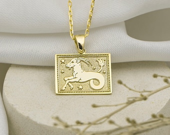May include: Gold necklace with a square pendant featuring a detailed depiction of the Capricorn zodiac sign.
