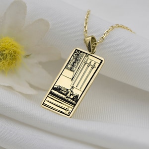 Puede incluir: Un collar de oro con un colgante que representa la carta del tarot Cuatro de Espadas. La carta está representada en blanco y negro sobre un fondo dorado.