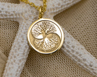 May include: A gold necklace with a round pendant featuring a tree of life design. The necklace is displayed on a white starfish and beige fabric.