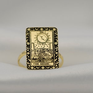 Puede incluir: Anillo de oro con un dise&ntilde;o rectangular negro que presenta la carta del tarot 'La Luna'. La carta representa una luna creciente, dos torres, un perro y un cangrejo.