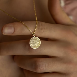 May include: A gold necklace with a round pendant featuring a detailed geometric design.