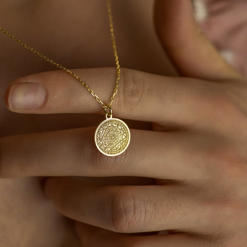 May include: A gold necklace with a round pendant featuring a detailed geometric design.
