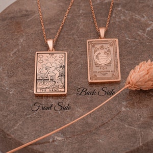 May include: A rose gold necklace with a pendant featuring the The Star tarot card on the front and a decorative design on the back.