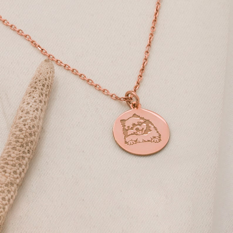 May include: A rose gold necklace with a round pendant featuring an engraved image of a dog. The pendant is hanging on a delicate chain.