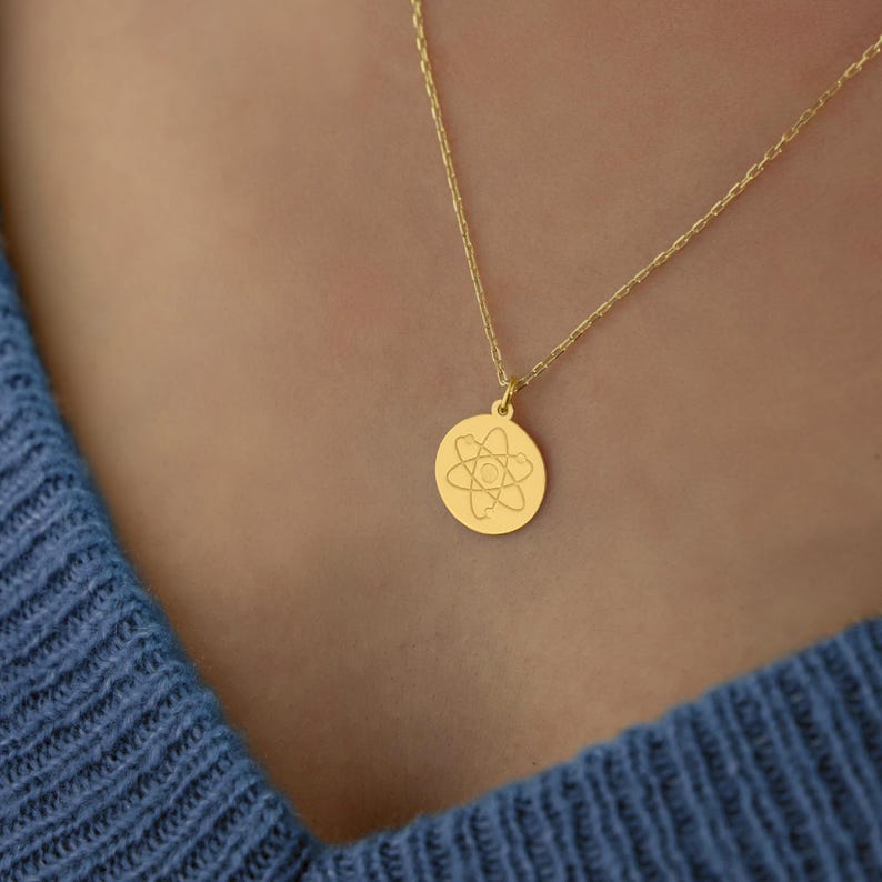 May include: A gold necklace with a round pendant featuring an engraved atom symbol.
