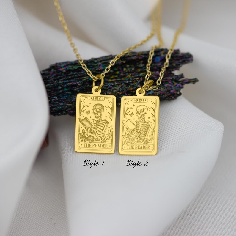 Op de afbeelding: Twee gouden kettingen met rechthoekige hangers met een skelet dat een boek leest. De hangers zijn gegraveerd met de woorden "The Reader" en "Death".
