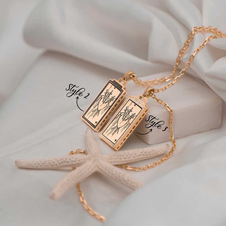 Puede incluir: Dos colgantes de oro con una imagen en blanco y negro de un coraz&oacute;n atravesado por espadas. Los colgantes est&aacute;n en una cadena de oro y est&aacute;n etiquetados como "Style 2" y "Style 3".