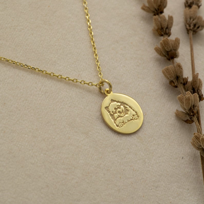 May include: Gold necklace with a round pendant featuring a dog's face in a cutout design.