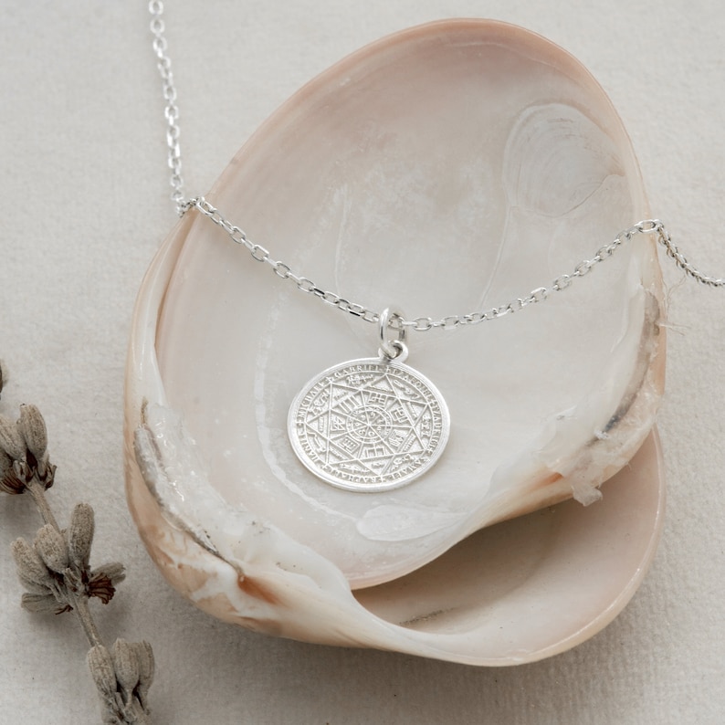 May include: A silver necklace with a circular pendant featuring an intricate geometric design. The pendant is surrounded by a circle of smaller symbols. The necklace is displayed on a white background.