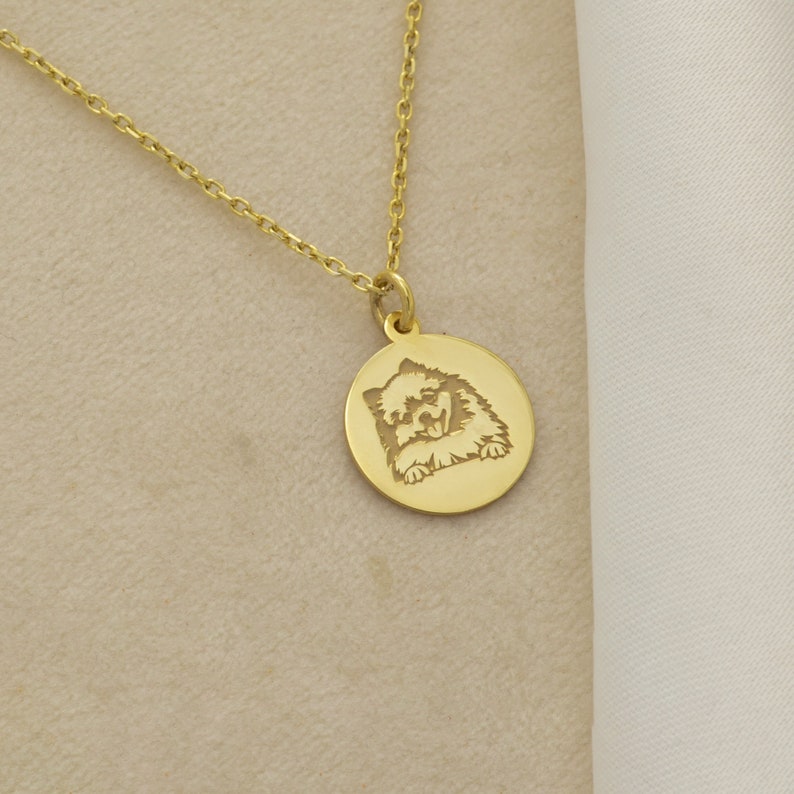 May include: A gold chain necklace with a round pendant featuring an engraved image of a dog.