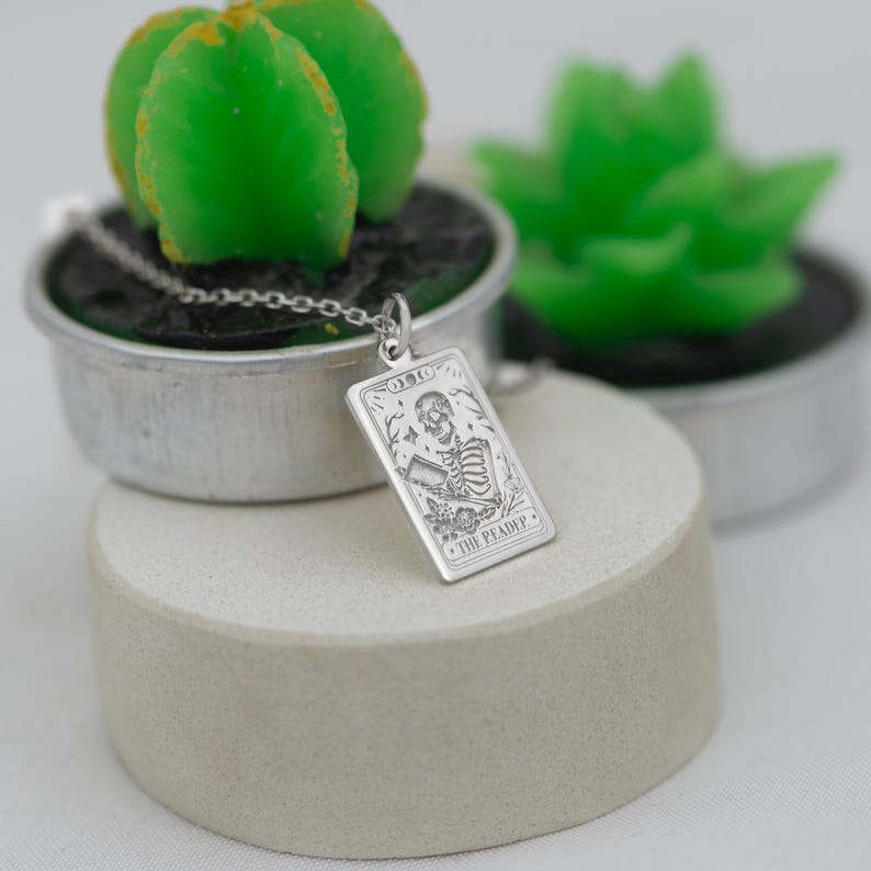 Op de afbeelding: Een zilveren ketting met een rechthoekige hanger met een skeletfiguur en de tekst "The Pleader".
