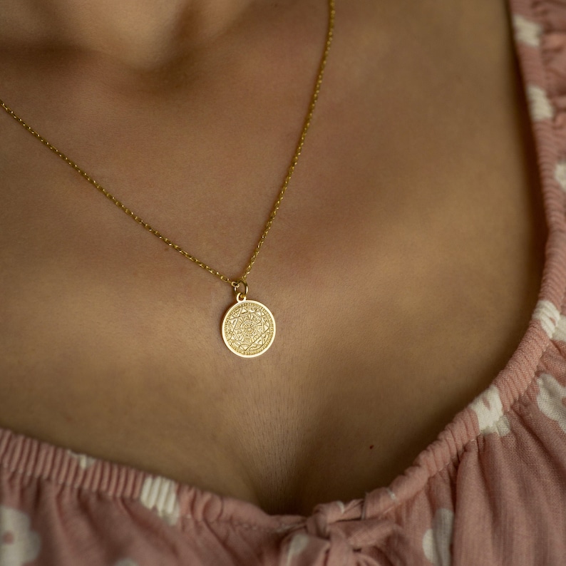 May include: A gold chain necklace with a round pendant featuring an intricate design.