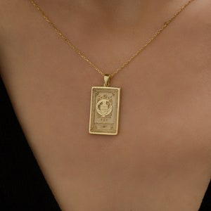 May include: A gold necklace with a rectangular pendant featuring an intricate design. The pendant has a raised image of a vase with flowers and the number 193. The necklace is on a model's neck.