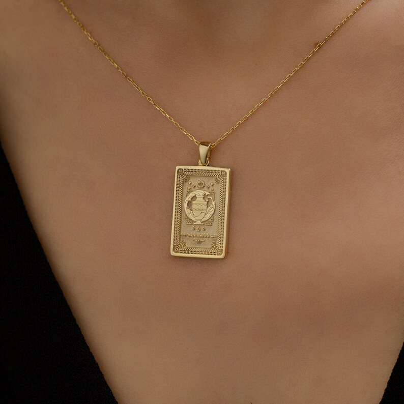 May include: A gold necklace with a rectangular pendant featuring an intricate design. The pendant has a raised image of a vase with flowers and the number 193. The necklace is on a model's neck.