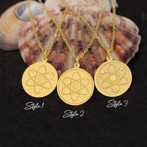 May include: Three gold necklaces with atom pendant charms. The pendants are round and feature a stylized atom design. The necklaces are labeled "Style 1", "Style 2", and "Style 3".