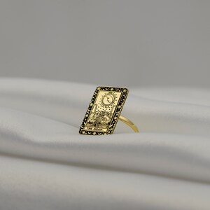 Puede incluir: Anillo de oro con un dise&ntilde;o de esmalte negro de la carta del tarot La Luna. La carta representa una luna creciente, dos torres, un perro y un cangrejo.