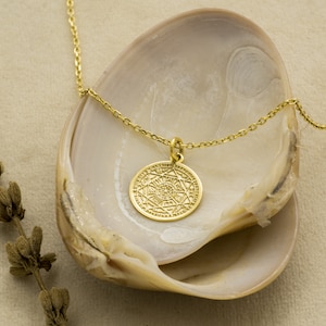 May include: A gold necklace with a round pendant featuring a detailed geometric design. The pendant is in the shape of a circle with a star inside.