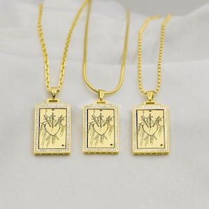 Puede incluir: Tres collares de oro con colgantes a juego. Cada colgante es un marco rectangular de oro con una imagen en blanco y negro de la carta del tarot Tres de Espadas. El marco est&aacute; bordeado con peque&ntilde;as piedras transparentes.
