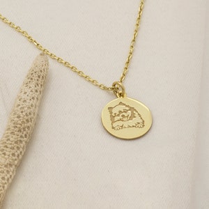 May include: A gold chain necklace with a round pendant featuring an engraved image of a dog. The dog is looking up with its tongue sticking out.