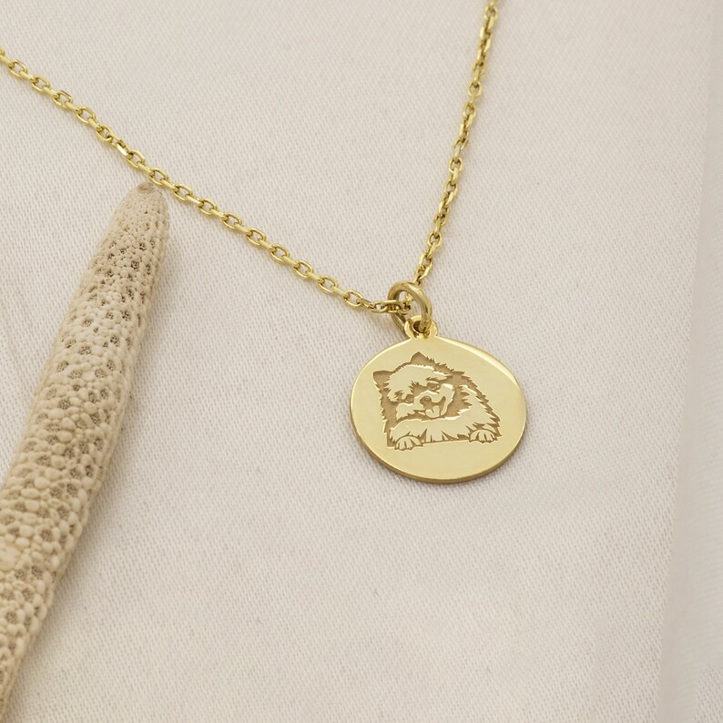 May include: A gold chain necklace with a round pendant featuring an engraved image of a dog. The dog is looking up with its tongue sticking out.