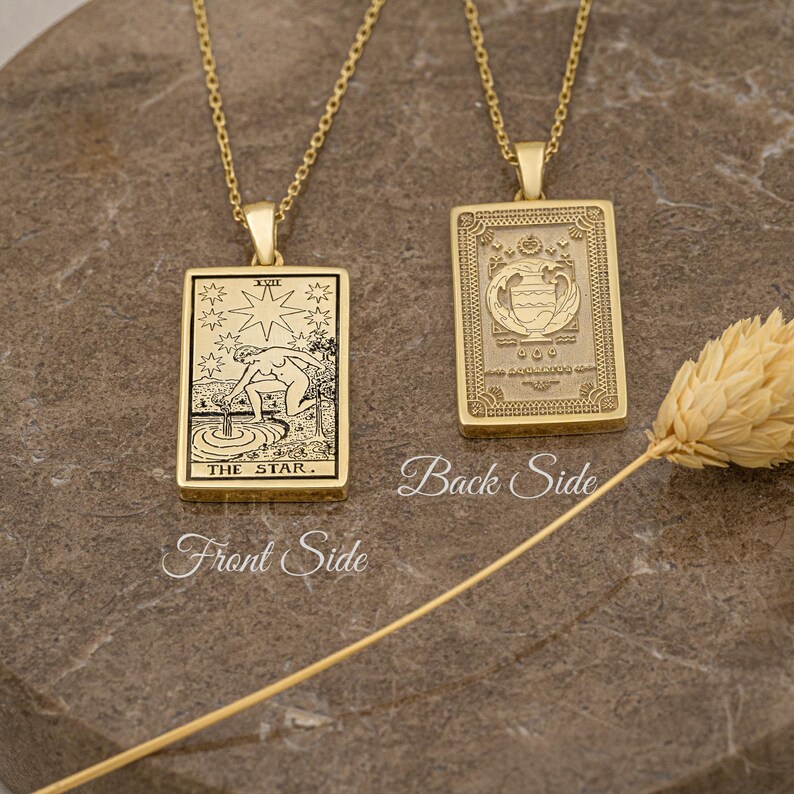 May include: Gold necklace with a pendant featuring a tarot card design. The front of the pendant shows the Star card with a woman pouring water from two jars. The back of the pendant has a simple design.