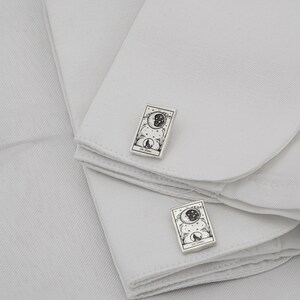 May include: Silver cufflinks with a rectangular design featuring a crescent moon, stars, and a howling wolf. The cufflinks are set against a white background, showcasing the intricate details of the celestial and animal imagery.