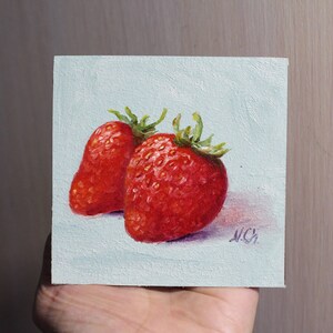 Two red strawberries painted on a light blue canvas. The strawberries are in focus and the background is blurred. The painting is signed .