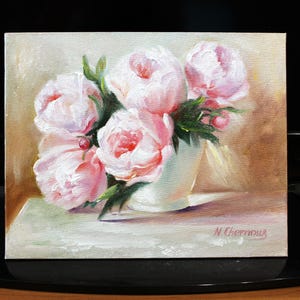 Peonies oil painting of a bouquet of pink peonies in a white vase. The flowers have multiple layers of petals and green leaves. The background is a soft, neutral color, and the painting is signed in the bottom right corner. The painting is signed "N. Chernous" in the bottom right corner.