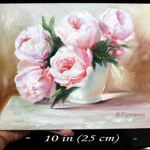 Peonies oil painting of a bouquet of pink peonies in a white vase. The flowers have multiple layers of petals and green leaves. The background is a soft, neutral color, and the painting is signed in the bottom right corner.