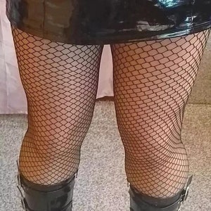 Puede incluir: Un par de botas negras de charol con hebillas plateadas. Las botas tienen una punta puntiaguda y un tacón alto. Las botas se llevan con medias de rejilla negras.