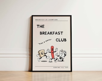 May include: A framed poster with a black border displays a retro illustration. The poster reads "The Breakfast Club" with "Rise & Shine" below. Cartoon characters of toast, a sausage, and a coffee cup are shown. The words "Breakfast of Champions" and "Serving All Day" are also included.