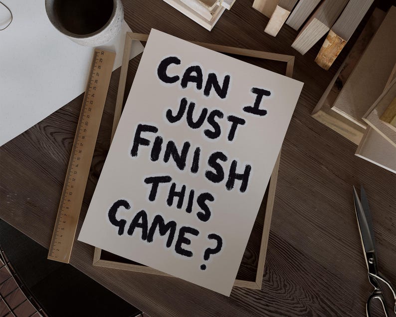 May include: A framed print with the text "Can I just finish this game?" written in black marker on a white background.