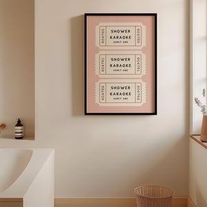 May include: A framed art print featuring three vintage-style tickets with the text "SHOWER KARAOKE ADMIT ONE" in black. The tickets are set against a light pink background within a black frame. The artwork is displayed on a neutral-toned wall.