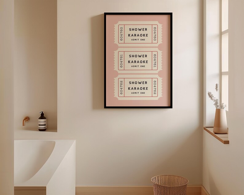 May include: A framed art print featuring three vintage-style tickets with the text "SHOWER KARAOKE ADMIT ONE" in black. The tickets are set against a light pink background within a black frame. The artwork is displayed on a neutral-toned wall.