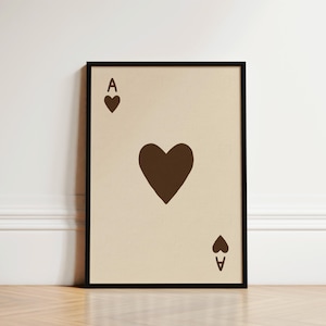 May include: Framed art print featuring the Ace of Hearts playing card. The card has a beige background with a large brown heart in the center, and smaller brown hearts and the letter "A" in the corners. The frame is black.