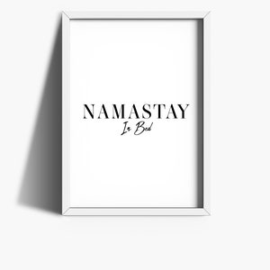 May include: A white framed print with the text "NAMASTAY In Bed" in black lettering.
