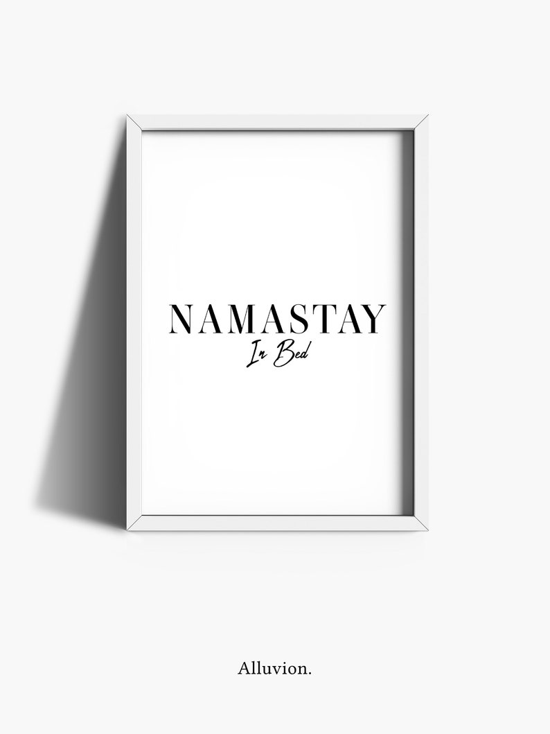 May include: A white framed print with the text "NAMASTAY In Bed" in black lettering.