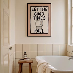 May include: A bathroom with a white bathtub, a wooden stool, and a framed print on the wall that says "Let the good times roll" with a cartoon image of a toilet paper roll.