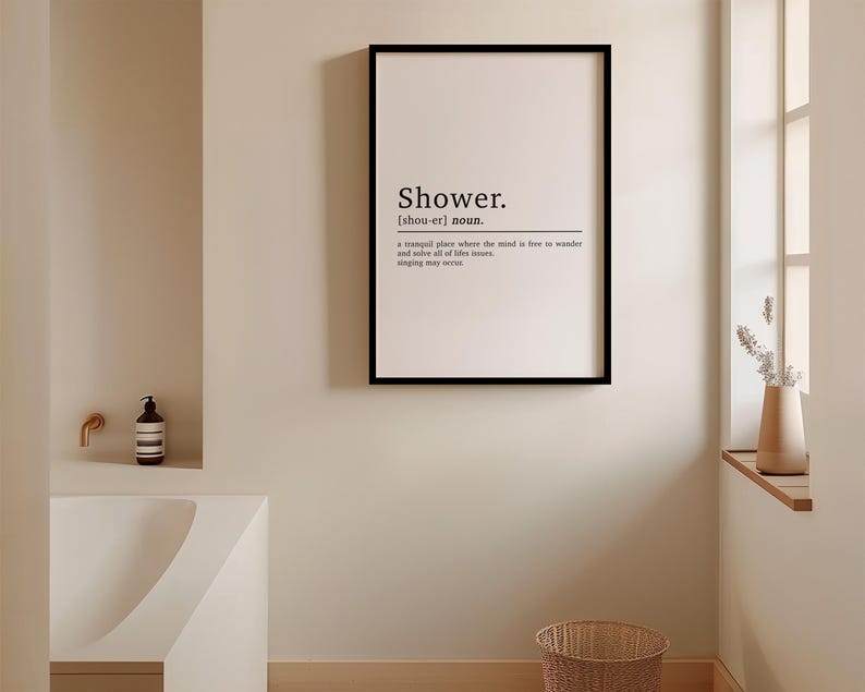 May include: A black framed print with the word "Shower" in a white sans-serif font. The definition of the word is below, "a tranquil place where the mind is free to wander and savour all of life's treasures, singing may occur."