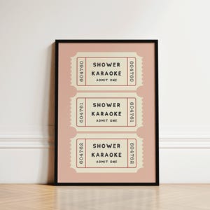 May include: A framed print featuring three vintage-style tickets. Each ticket, in a cream color with a pink background, reads "SHOWER KARAOKE ADMIT ONE." The tickets have a serrated edge and a serial number. The frame is black.