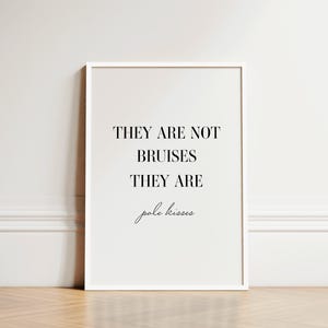 May include: A white framed print with the text "They are not bruises they are pole kisses" in black font.