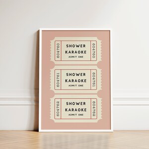 May include: A framed print featuring three vintage-style tickets. Each ticket, in a cream color with red accents, reads "Shower Karaoke, Admit One." The tickets are arranged on a pink background.