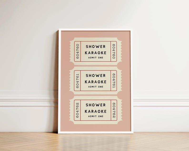 May include: A framed print featuring three vintage-style tickets. Each ticket, in a cream color with red accents, reads "Shower Karaoke, Admit One." The tickets are arranged on a pink background.