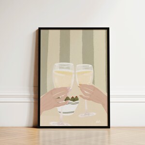 May include: Art print in a black frame showing two champagne flutes clinking, filled with a golden liquid. The artwork includes a small bowl of olives and a striped background. The hands are holding the glasses in a celebratory toast.