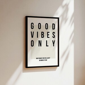 May include: Black framed print with white background and the text "GOOD VIBES ONLY" in black. The text is arranged in a grid pattern. Below the text is the phrase "WHAT MAKES YOU FEEL ALIVE? DO MORE OF THAT."