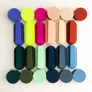 May include: A selection of colourful bottle stoppers and handles in shades of blue, green, pink, and neutral tones. The stoppers are round, while the handles are oval, all with a ribbed design. A vibrant and stylish assortment.