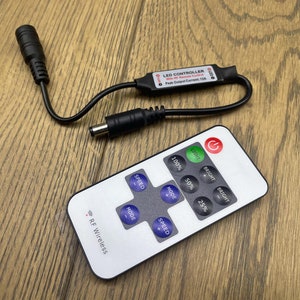 Op de afbeelding: Een zwarte LED-controller met een afstandsbediening. De controller heeft een rood label met de tekst "LED CONTROLLER" en de afstandsbediening heeft knoppen voor "SPEED", "MODE", "BRIGHT" en "LIGHT".