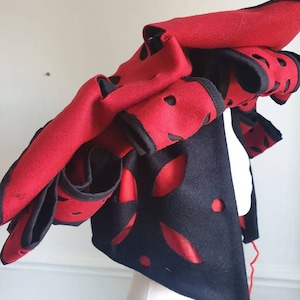 Puede incluir: Un sombrero de fieltro rojo y negro con dise&ntilde;os recortados. El sombrero est&aacute; doblado y tiene una larga cuerda roja atada.