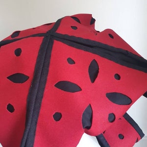 Puede incluir: Sombrero de fieltro rojo con dise&ntilde;os recortados en negro y ribete negro.